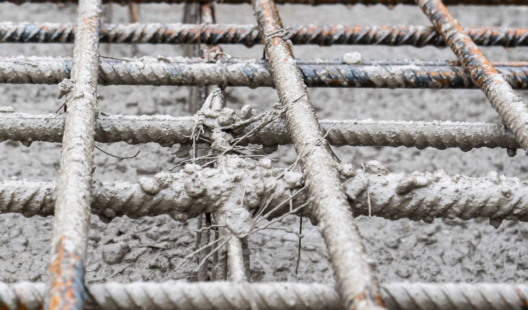 Armeringsjern i kvadratisk mønster dekket av fersk betong, med enkelte synlige rustflekker på metallet.