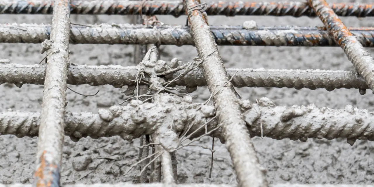 Armeringsjern i kvadratisk mønster dekket av fersk betong, med enkelte synlige rustflekker på metallet.