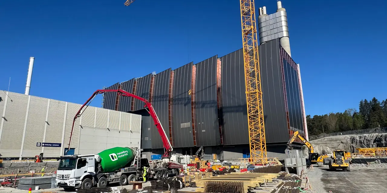 Byggeplass med stort industribygg under oppføring, inkludert kraner og betongbil.