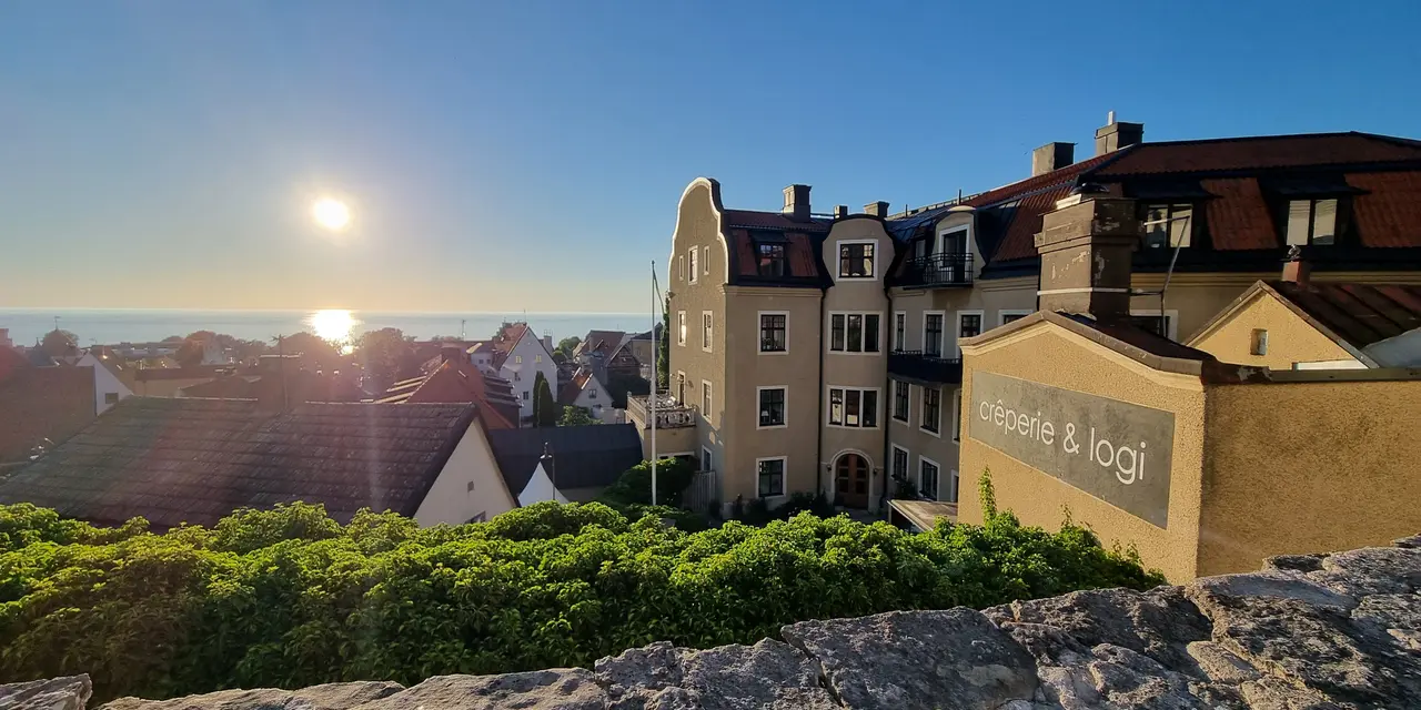 Vy över hustak i Visby och hav vid solnedgången, med byggnader i olika material som framträder tydligt.